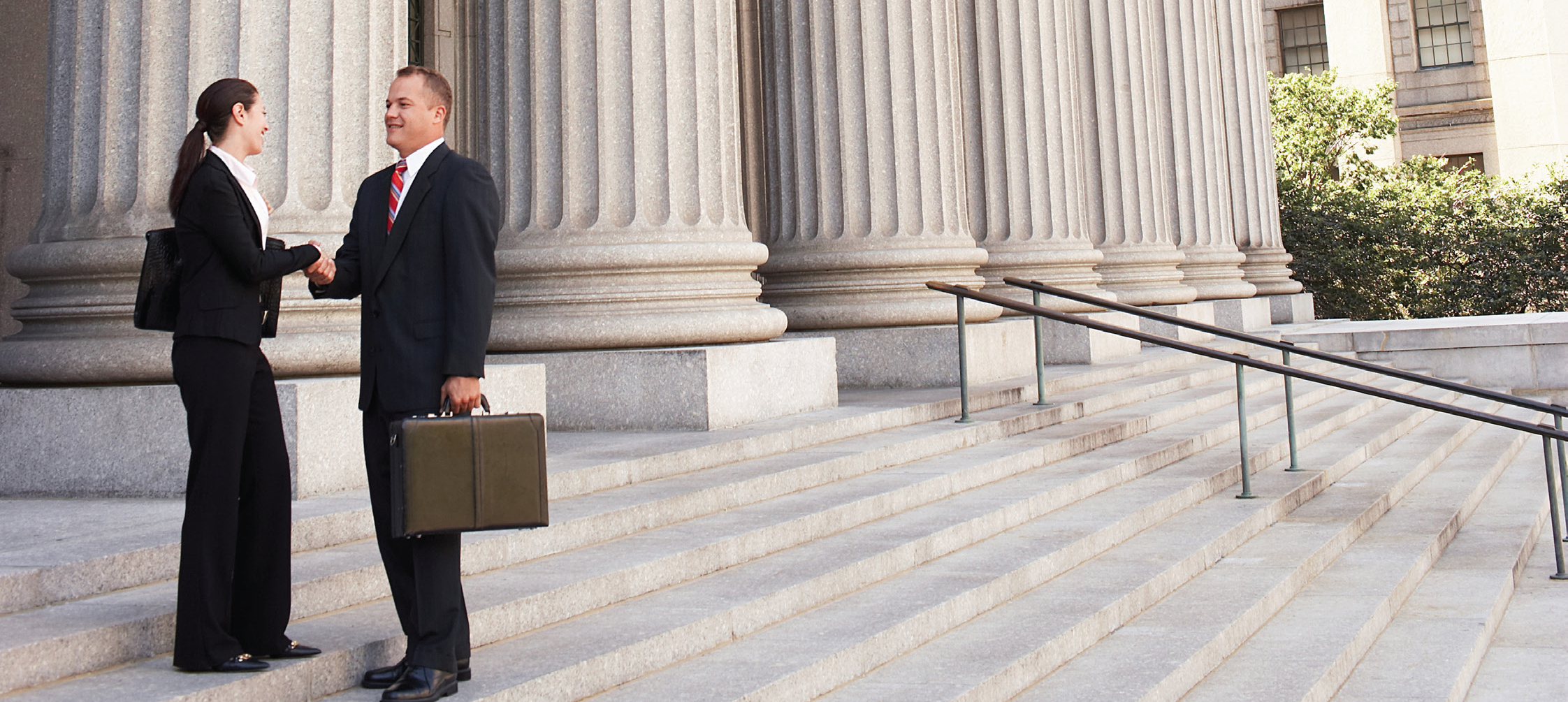 An attorney holding a breifcase, shaking the hand of a woman in front of a courthouse